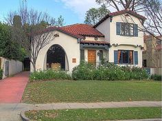 a white house with blue shutters on the front and red roof, along side a sidewalk