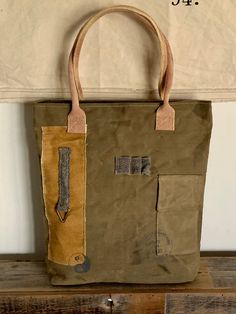 "Vintage military upcycled tent canvas tote handbag Colorations: Olive green, khaki gold, gray & cream Writing: Gray Vintage brass hardware Cream/wine double handles *Please note: All materials are upcycled. Colorations and fabric shading/distressing will vary. All fabric is best quality.  Specifications: 16x17x4\" 9\" double handle Top zippered closure Exterior back zippered pocket, front fold pocket  Interior 3 pockets (1 zippered) Key clip  Hand/paw ying/yang Unconstructed, but sturdy canvas" Khaki Canvas Tote Bag With Canvas Lining, Khaki Canvas Tote Bag, Khaki Canvas Tote Bag With Leather Handles, Green Canvas Tote Bag For Outdoor Use, Green Tote Canvas Bag For Outdoor, Utility Khaki Bag For Daily Use, Khaki Utility Bag For Daily Use, Rectangular Khaki Canvas Bag With Handles, Khaki Canvas Bag With Handles