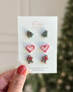 a person holding up three pairs of heart and arrow earrings in front of a christmas tree