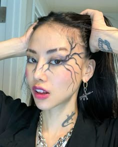 a woman with tattoos on her face and hands behind her head, wearing a black shirt