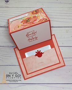 an open card box with a red flower inside on a white wooden surface, showing the front and back sides