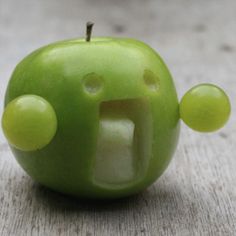 an apple with its mouth open and two green balls in the shape of people's faces