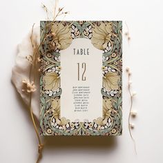 a table number card on top of a white surface with dried flowers and leaves around it