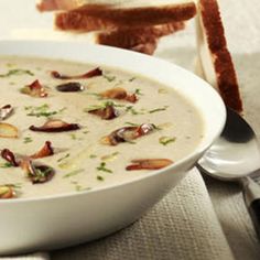 a white bowl filled with soup next to a slice of bread on a tablecloth