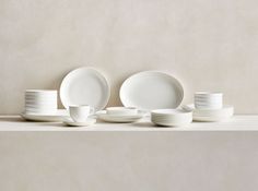 white dishes and cups are arranged on a shelf in front of a beige wall,