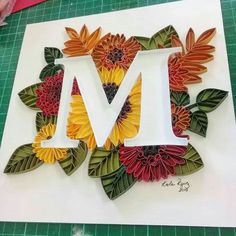 the letter m is made out of paper and has sunflowers, leaves, and flowers on it