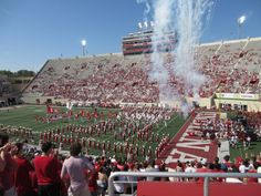 a group of people standing on top of a field next to a football stadium filled with fans