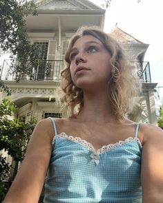 a woman standing in front of a house with her hand on her hip and looking up at the sky