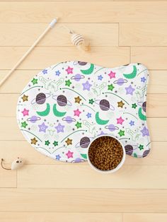 a dog bowl mat with space themed design on it, next to two bowls and spoons