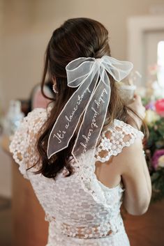 the back of a woman's head wearing a wedding dress with a ribbon around it