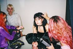 three women are sitting on the floor with hair dryers in their hands and one woman is combing her hair