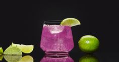 a purple drink with limes and two lime wedges next to it on a reflective surface