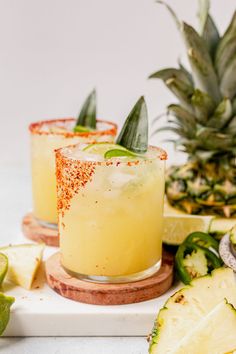 two pineapple margaritas with garnish on the rim, surrounded by sliced pineapple slices