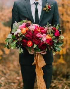 a man wearing a suit and tie holding a bouquet with red flowers in his hands