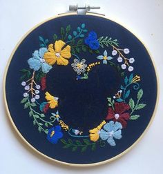 an embroidered heart on a blue background with flowers and leaves in the center is shown