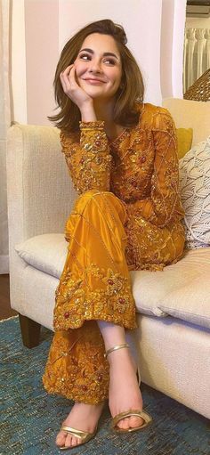 a woman sitting on top of a couch next to a white chair and smiling at the camera