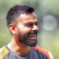 a man with a beard smiles at the camera while wearing an orange and grey shirt