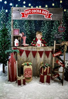 a little boy sitting at a bar with christmas decorations on the table and behind him is a sign that says hot cocoa bar