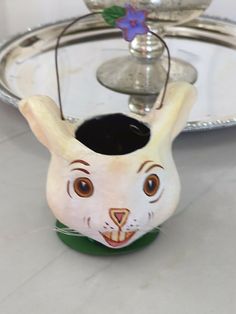 a white rabbit head vase sitting on top of a silver tray next to a candle holder