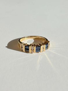 a yellow gold ring with blue and white stones on the outside, sitting on a plain surface