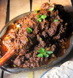 a dish with meat and vegetables in it sitting on a table next to pita bread