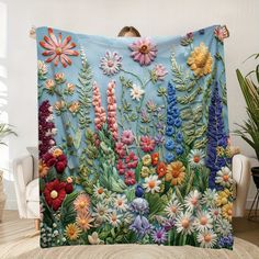 a blue blanket with flowers on it is hanging in front of a chair and potted plant