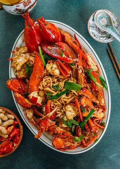 a plate full of noodles and lobsters with chopsticks next to it on a table