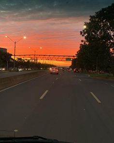 the sun is setting on an empty road with cars driving down it and trees lining both sides