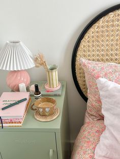 a nightstand with a lamp, notebook and other items on it next to a bed