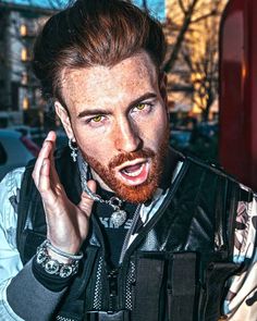 a man with a beard and piercings talking on a cell phone while wearing a leather vest