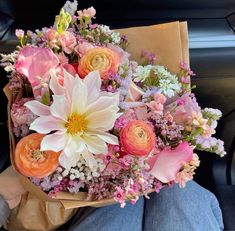 a bouquet of flowers sitting in the back seat of a car with someone holding it