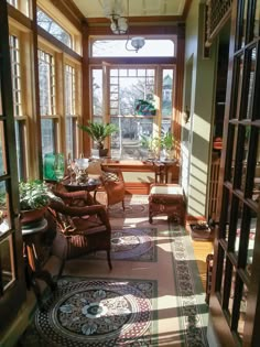 the sun shines through two large windows into a room with chairs, tables and potted plants