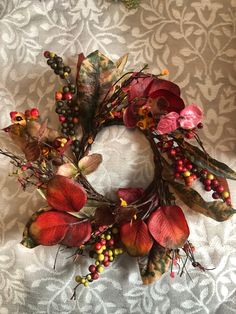 a wreath made out of leaves and berries on a white tablecloth with an ornate pattern