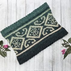 a green and white rug sitting on top of a wooden floor next to pink flowers