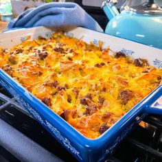 a blue casserole dish sitting on top of an oven with food in it