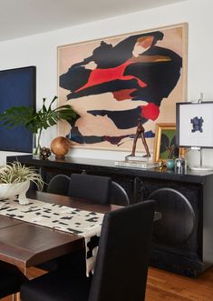 a dining room table with black chairs and a large painting on the wall behind it