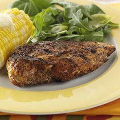 grilled meat, corn on the cob and salad are served on a plate