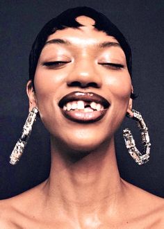 a woman with her eyes closed and wearing large earrings on top of her head, smiling