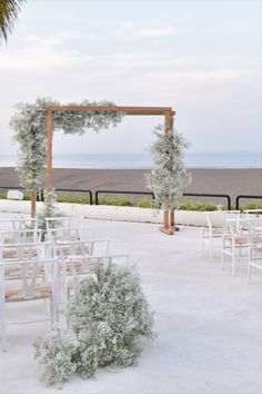 an outdoor wedding setup with white chairs and greenery on the aisle, overlooking the beach