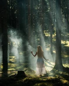 a woman standing in the middle of a forest surrounded by fog and sunbeams