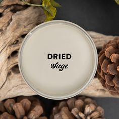 a glass jar with the word dried sage on it next to pine cones and branches