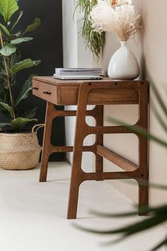 a wooden table topped with a white vase filled with flowers next to a potted plant