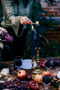 a woman lighting a candle on top of a table with fruit and candlesticks