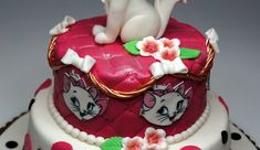 the cake is decorated with pink and white designs on it's sides, along with a cat figurine sitting on top