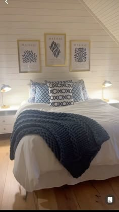 a bed with white sheets and blue blankets in a room next to two framed pictures on the wall