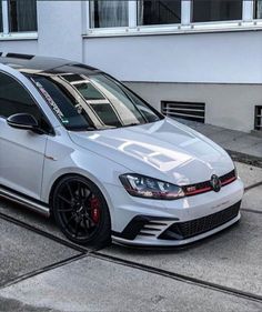 the white volkswagen golf gtr is parked in front of a building with black rims