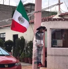 a man standing next to a red car holding a mexican flag