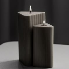 two candles sitting next to each other on top of a white table with dark background