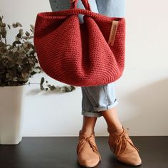 a woman holding a red knitted bag in front of her legs and shoes on the floor