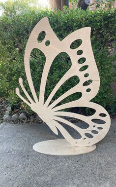 a wooden sculpture of a butterfly sitting on top of a cement ground next to a bush